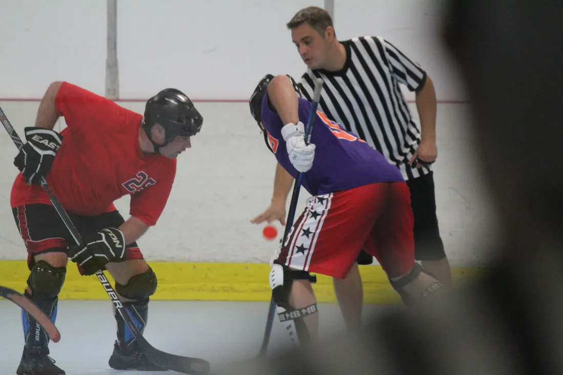A referee dropping the ball for a face-off between two adult players at the Bridgeville HockeyPlex